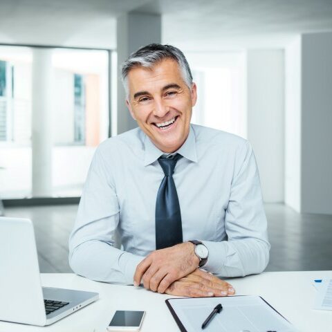 Confident handsome businessman sitting at office desk and smiling at camera