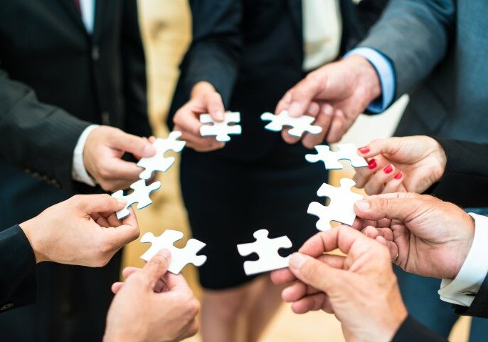 Teamwork - a group of eight business people assembling a jigsaw puzzle - representing team support and help concepts